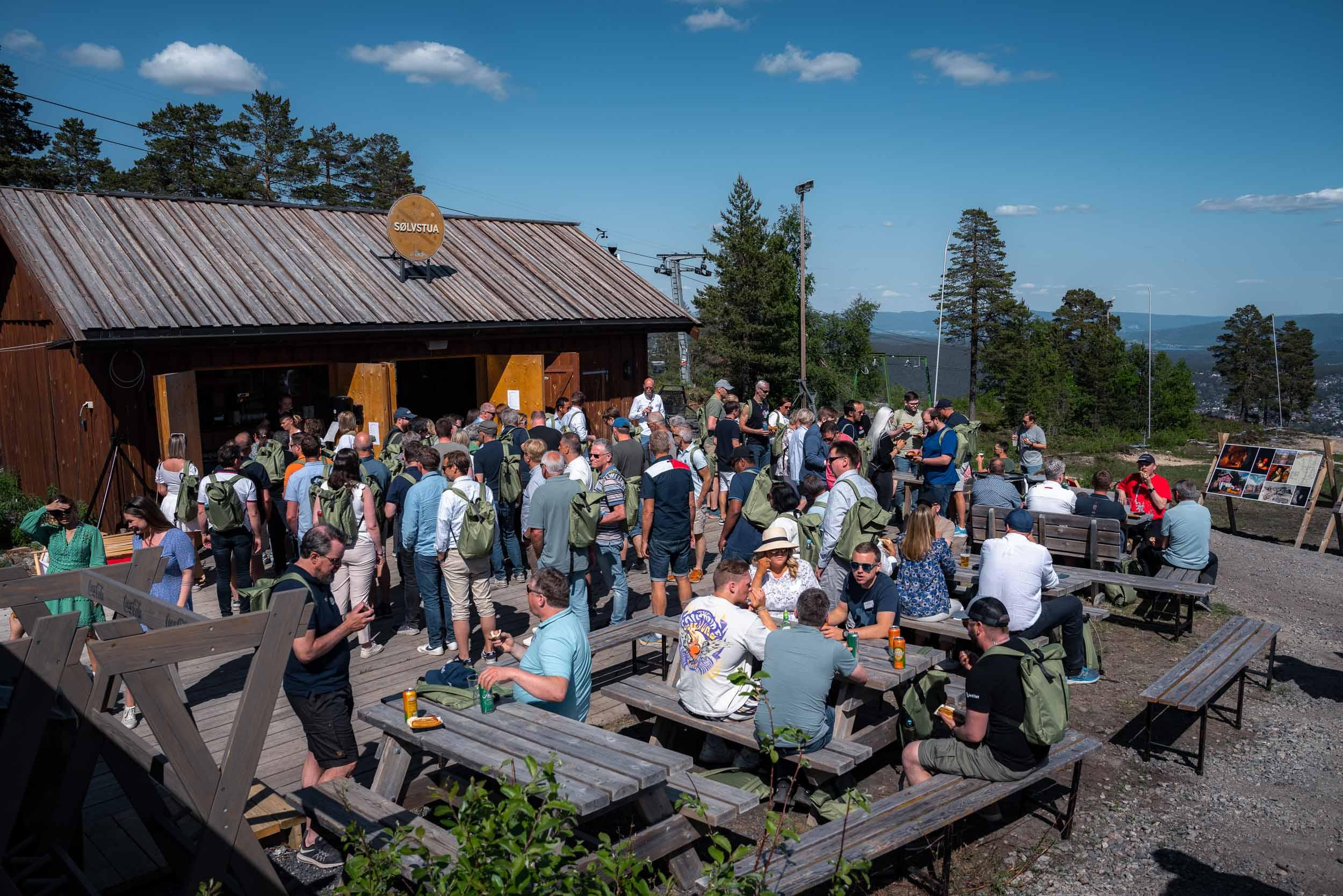Gjester samlet utendørs ved bordene under en sommerfest